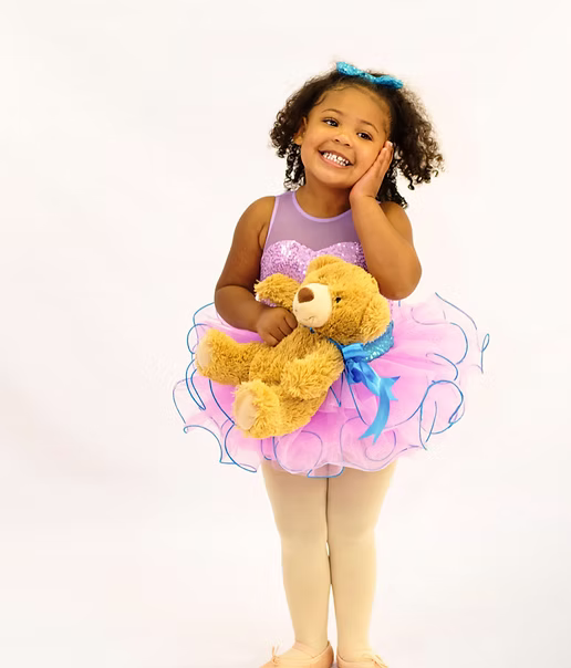 Young dancer in a purple tutu holding a teddy bear